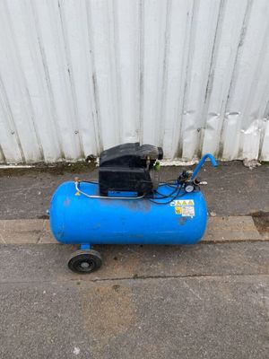 a blue air compressor sitting on the ground next to a white wall