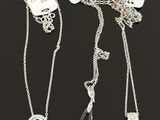three silver necklaces with tags on them on a black surface