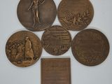 six bronze medallions of various types and sizes on a white surface