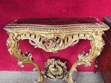 une console ancienne aux sculptures ouvragées, devant un mur rouge