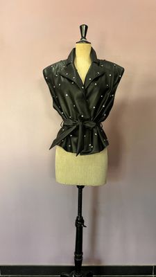 veste en cuir noir sur un mannequin, ornée de perles et d'un nœud papillon
