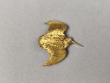 un gros plan d'une broche en forme d'oiseau dorée posée sur une surface blanche