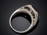 a close up of a ring with a red stone and diamonds