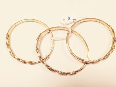 three gold bang bracelets on a white surface with a white object in the background