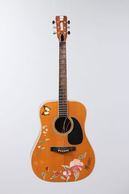 an orange guitar with flowers painted on it hanging from a white wall
