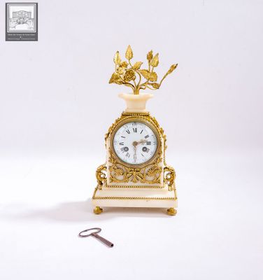 une petite horloge en or surmontée d'un oiseau, à côté d'une paire de ciseaux