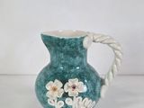 a green vase with flowers on it on a white table