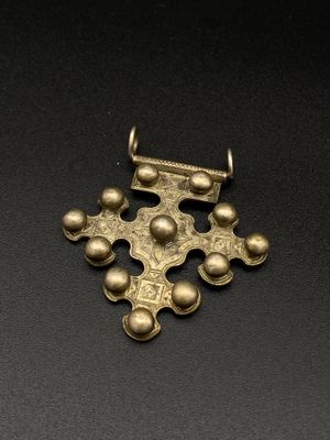 un pendentif en forme de croix en or orné de quatre boules et d'une chaîne, sur un fond noir