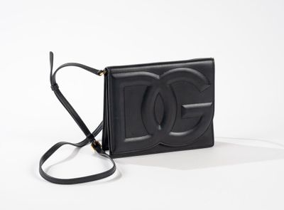 Le petit sac noir est posé sur une surface blanche et est muni d'une bandoulière noire.