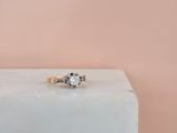 a gold engagement ring with two diamonds on top of a white marble block