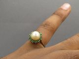 la main d'une femme tenant une bague ornée d'une perle et de pierres vertes
