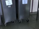 two stainless steel trash cans sitting on wheels in a room