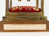 a gold clock with a red cushion on it