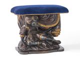une statue représentant un homme assis sur un tabouret avec un coussin bleu