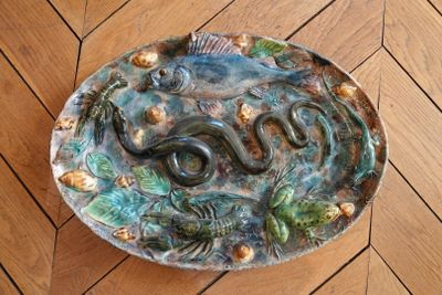 une assiette en céramique ornée d'un serpent, posée sur un plancher en bois