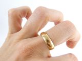 a person ' s hand holding a gold ring on a white surface