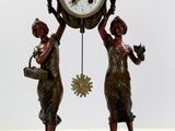 une statue représentant deux femmes tenant une horloge, posée sur un socle en marbre