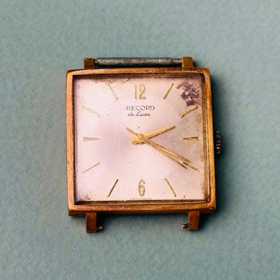 une petite montre carrée posée sur une surface bleue