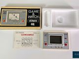 une console Game & Watch dans une boîte, à côté d'une manette de jeu