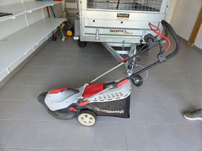 une tondeuse à gazon dans un garage, avec une remorque en arrière-plan