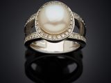 a white pearl and diamond ring on a black surface