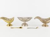 three silver and gold dishes and spoons sitting on a white surface