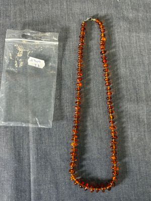 un collier de perles orange et un sac en plastique transparent posé sur un tissu gris