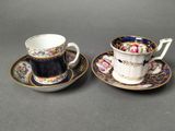 two cups and saucers with floral designs on them sitting on a table