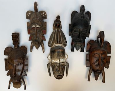 quatre masques en bois accrochés à un mur sur fond blanc