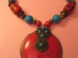 collier avec un pendentif rouge et des perles turquoise sur un fond rose