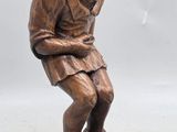 bronze statue of a man sitting on a stool with his hands on his knees