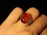 a woman ' s hand holding a ring with a red stone on it