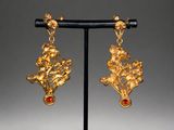 a pair of gold earrings with red stones on a stand