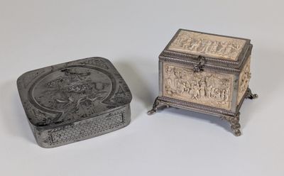 une paire de boîtes en argent ornées de sculptures, posées sur une surface blanche