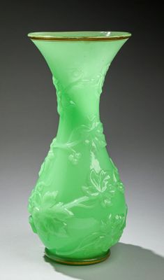 un vase en verre vert bordé d'or, posé sur une surface blanche