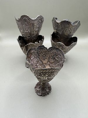 Suite de cinq zarfs en argent repoussé, ils posent sur une b…