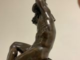 bronze statue of a woman sitting on a rock with her hands in the air