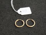 deux petites boucles d'oreilles en or en forme d'anneau posées sur une surface noire, avec une étiquette de prix