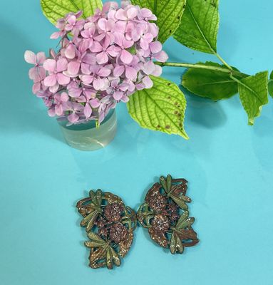 purple flowers in a vase and a pair of earrings on a blue surface