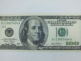 un billet de cent dollars posé sur une surface blanche