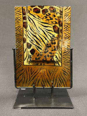 Assiette en verre à motifs zébrés et léopard, posée sur un support métallique, sur fond gris