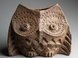 une image représentant un vase en pierre sur le dessus duquel est représenté un hibou