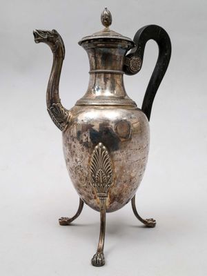 une théière ancienne en argent, dotée d'une anse noire, posée sur un socle