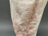 a close up of a mannequin head wearing a beige dress with pink embroidery