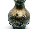 a bronze vase that is sitting on a white surface