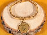 a close up of a gold bracelet with a coin on it