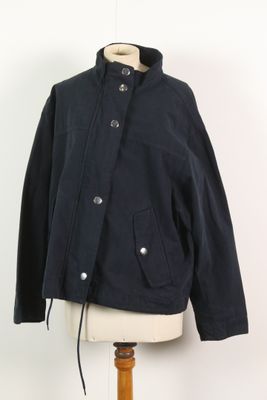 La veste est posée sur un support de mannequin, avec un mur blanc en arrière-plan.