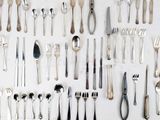 a lot of silver spoons and forks laid out on a table