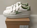 un gros plan sur une paire de baskets blanches et vertes posées sur une boîte