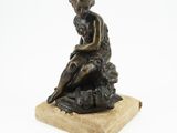 une vieille statue en bronze représentant un garçon assis sur un rocher